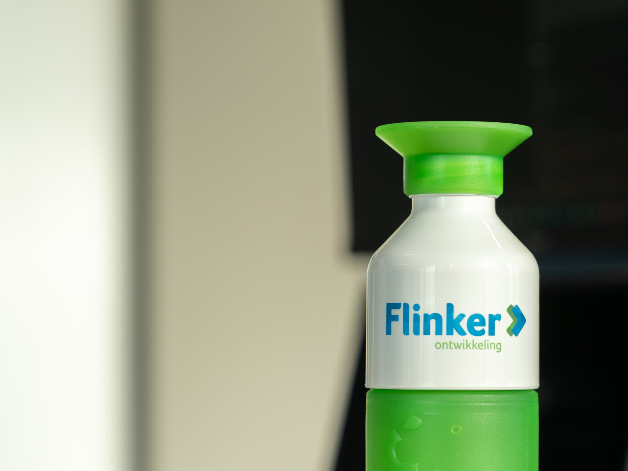 Groene Flinker Ontwikkeling-bidon op een bureau naast een werkende collega